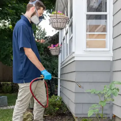 pest technician spraying exterior of home