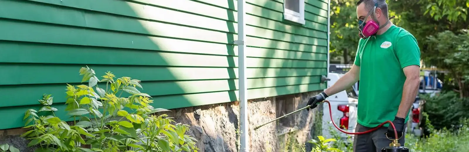 pest technician spraying exterior of home